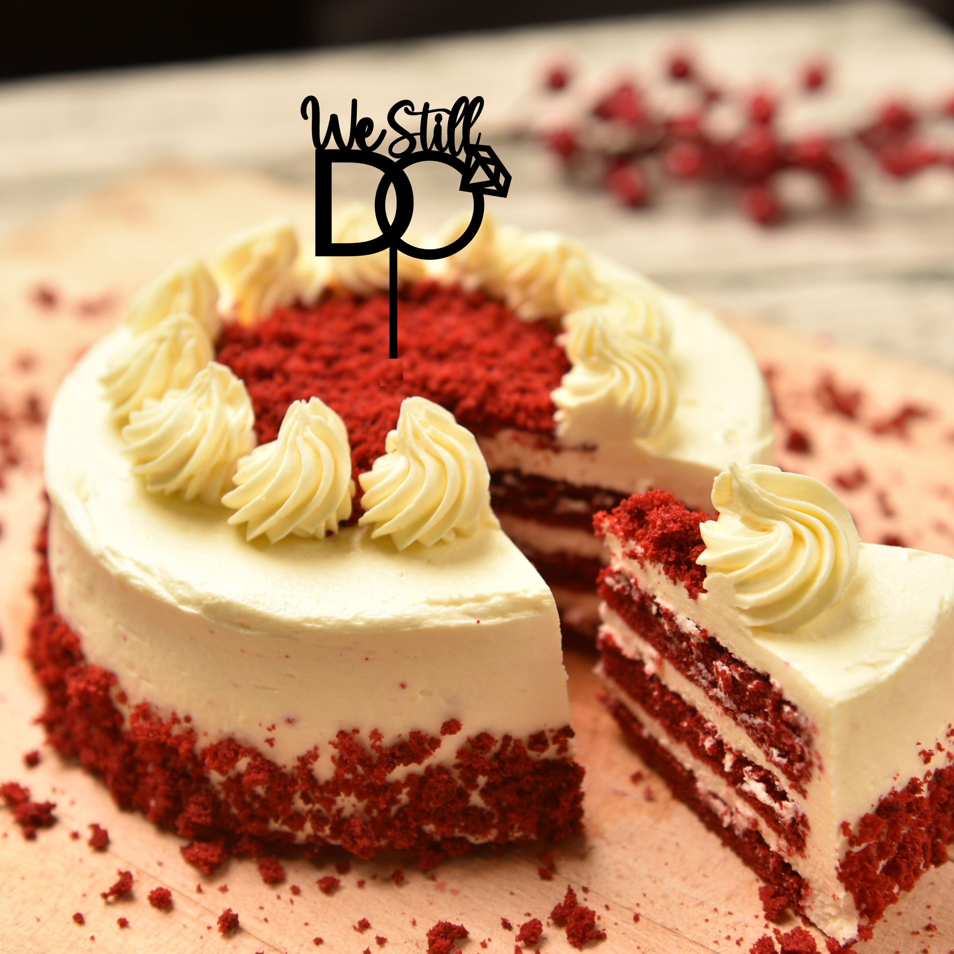 Celebratory cake topper with the words "we still do" in elegant script font in a red velvet cake.